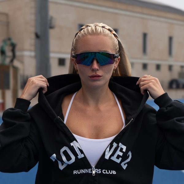 Runner in sport sunglasses pulling up the hood of her Zone 2 hoodie on a blue track