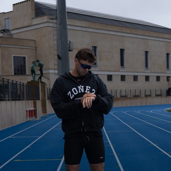 Runner in the hoodie checking his watch on a blue track